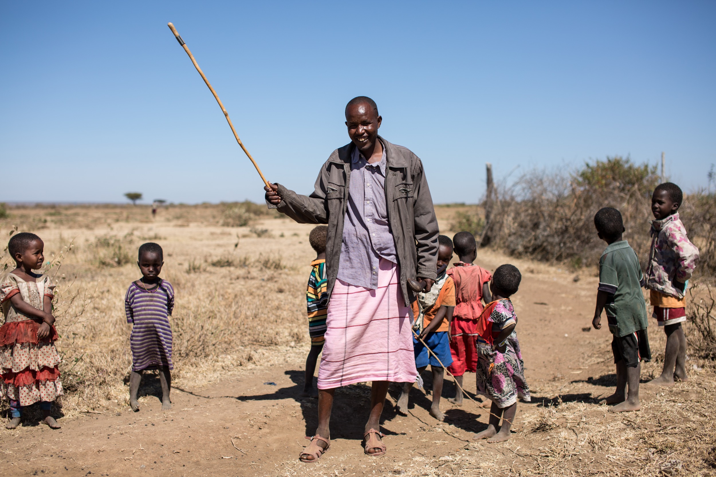 Older man with a stick with a group of kids outdoors on the barren land