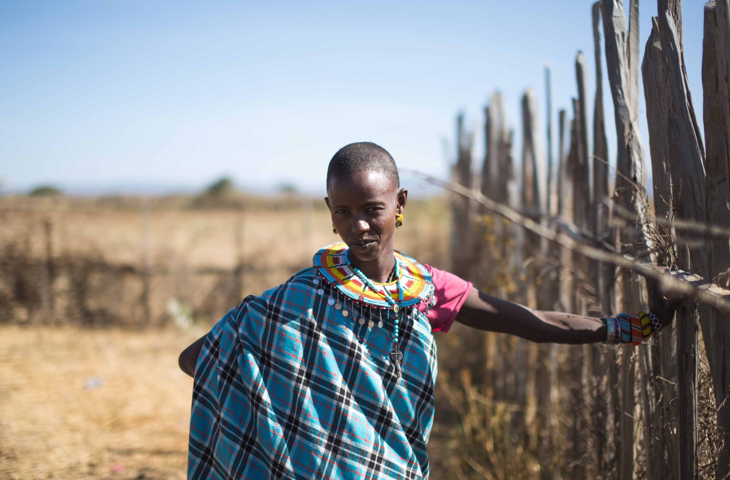 Samburu girl in tradtional dress leaning against wooden fence